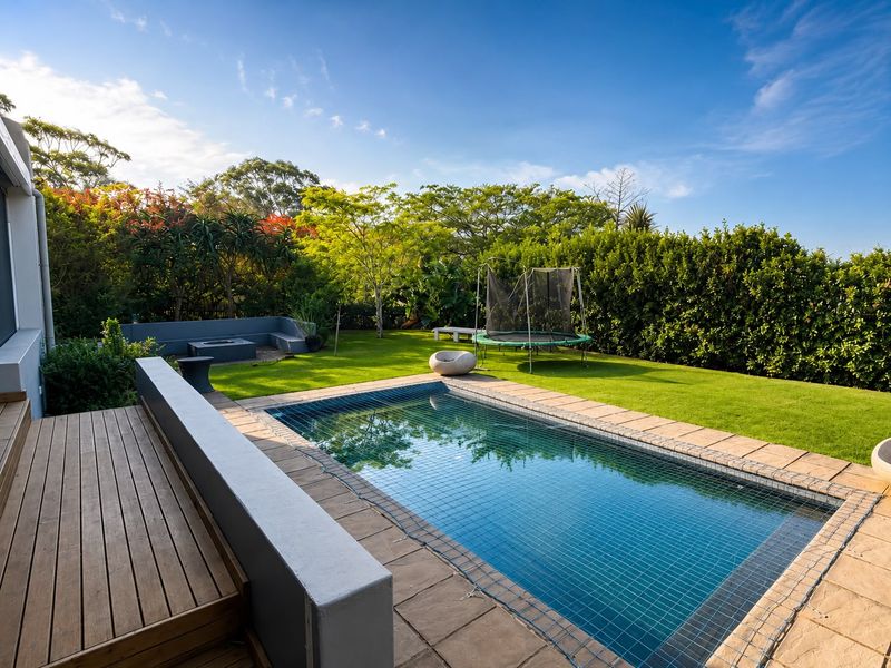 A well-maintained outdoor pool area featuring timber decking, a paved surround, and a built-in concrete bench set within a lush landscaped garden.