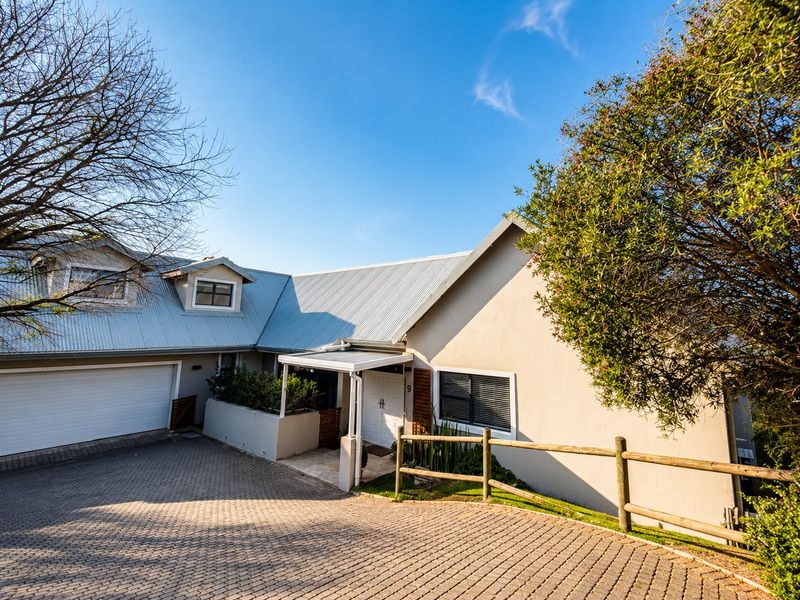 Front exterior view of a residential property featuring a paved driveway, garage, and covered entrance with a corrugated metal roof.