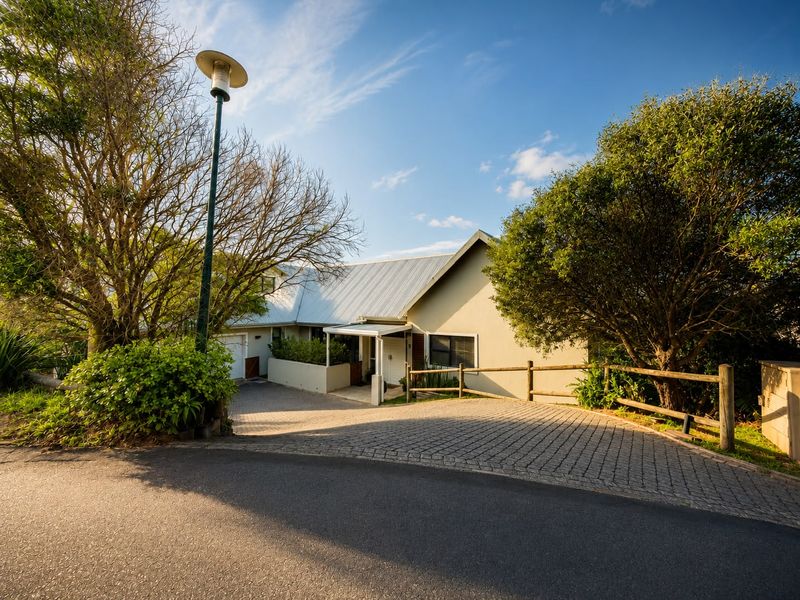 Front elevation of the property featuring a paved driveway, covered entrance, and a metal roof, surrounded by established trees and a timber fence.