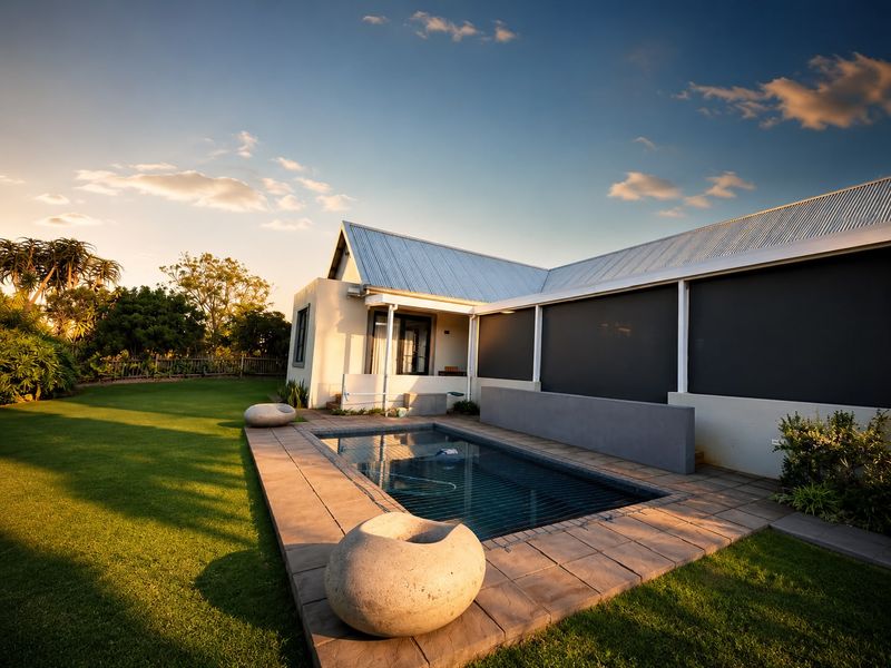 A well-maintained outdoor pool area featuring a paved deck, retaining wall, and modern metal roofing, set against a landscaped garden.