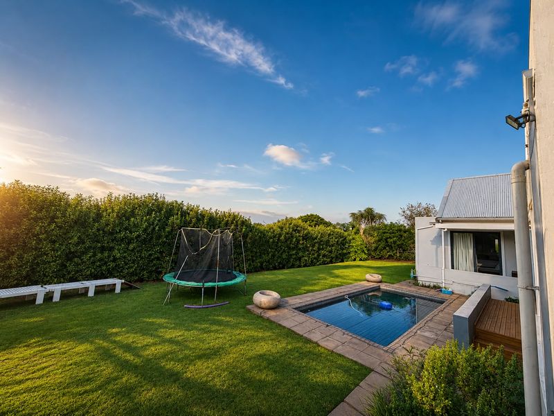 A well-maintained rear garden featuring a compact swimming pool with paved surround, timber decking, and established hedge privacy.