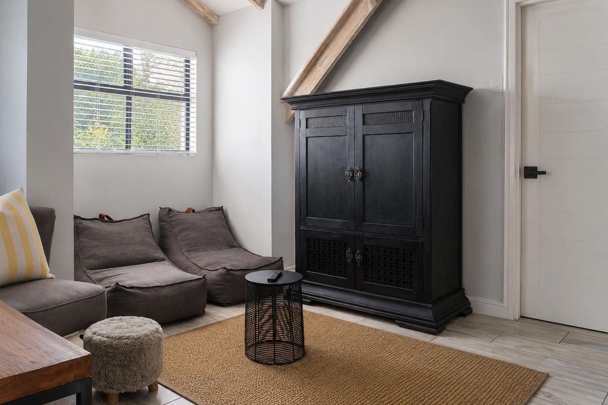 A cozy living area featuring exposed timber ceiling beams, neutral tiled flooring, and natural light through a window with venetian blinds.