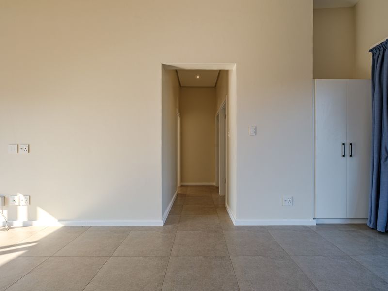 A clean, neutral-toned hallway featuring large-format floor tiles, recessed lighting, and a built-in storage cupboard, providing a bright and functional transition space.