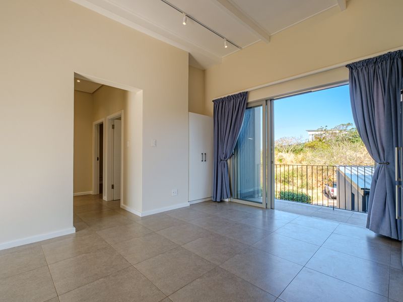 Bright open-plan living area featuring neutral tiled flooring, track lighting, and seamless access to a private balcony through large sliding glass doors.