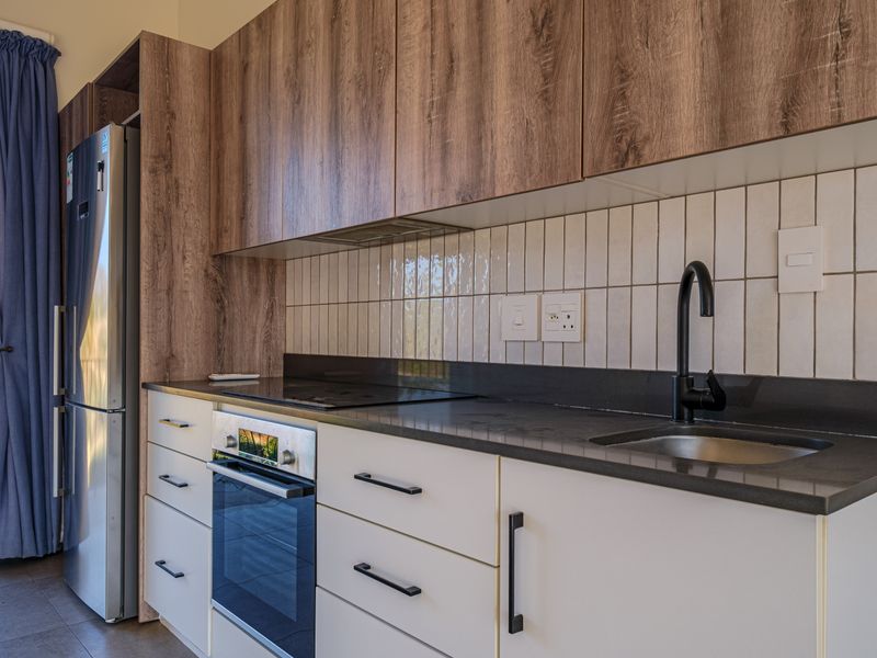 Modern kitchen featuring wood-grain upper cabinetry, white lower cabinets, stone countertops, a black mixer tap, and integrated stainless steel appliances.