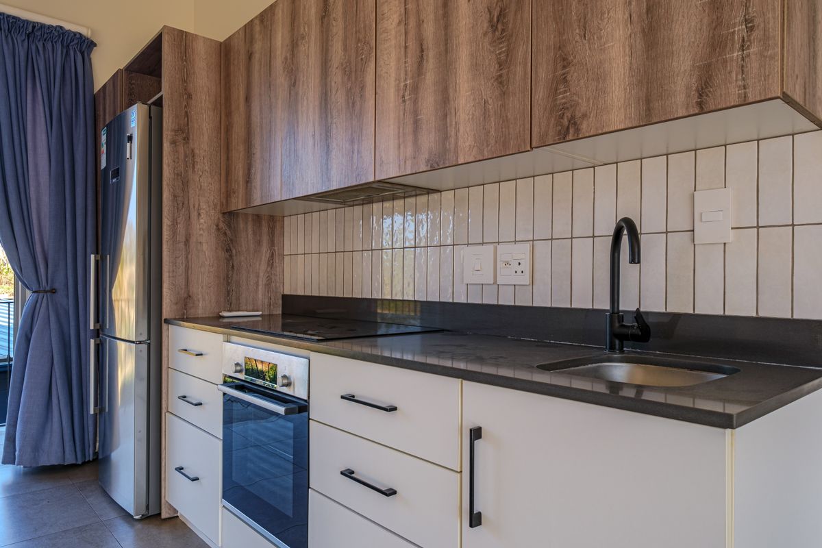 Modern kitchen featuring wood-grain upper cabinetry, white lower cabinets, stone countertops, a black mixer tap, and integrated stainless steel appliances.
