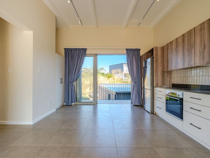 Modern open-plan kitchen and living area featuring sleek cabinetry, built-in appliances, tiled floors, and direct access to a balcony through sliding glass doors.