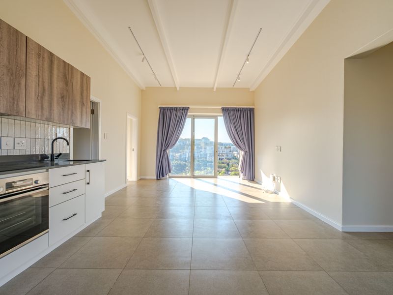 An open-plan living and kitchen area featuring modern cabinetry, built-in appliances, tiled flooring, and a sliding door leading to a balcony with views.