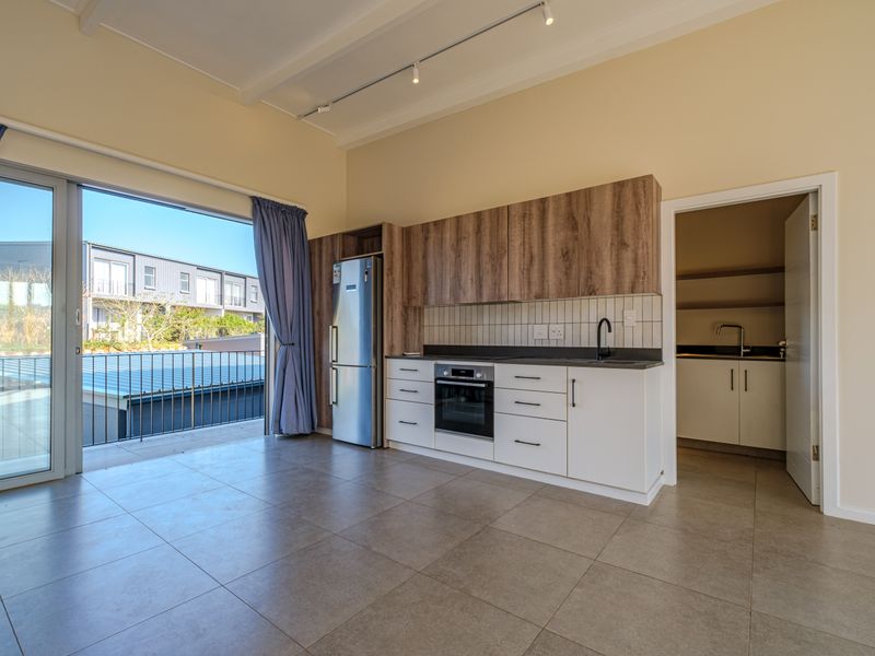 Modern open-plan kitchen and living area featuring tiled floors, built-in cabinetry, integrated oven, and direct access to a balcony, with an adjoining scullery.