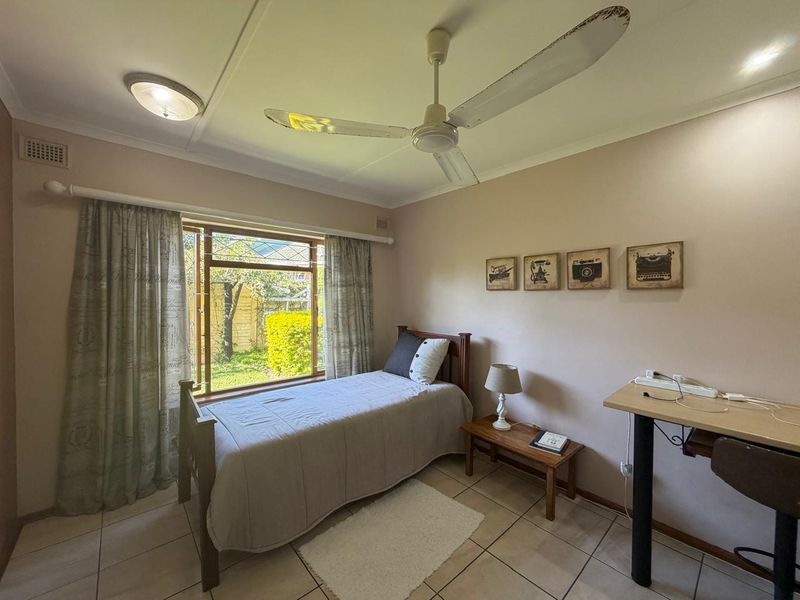 A functional bedroom featuring tiled flooring, a ceiling fan, and a window overlooking the garden area.