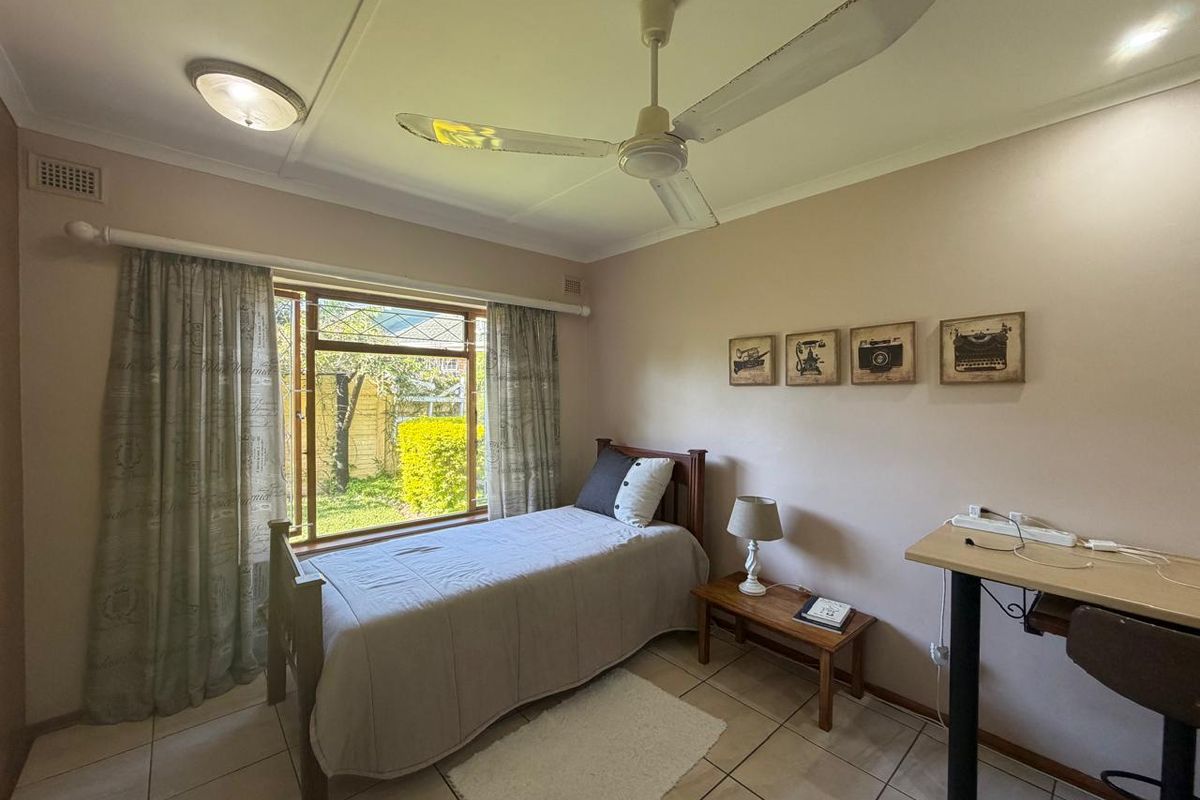A functional bedroom featuring tiled flooring, a ceiling fan, and a window overlooking the garden area.