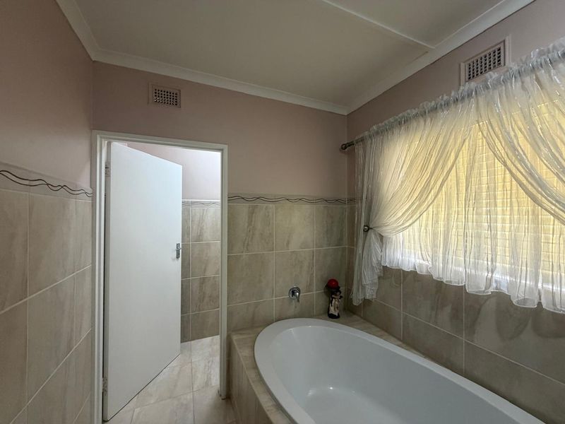 A functional bathroom featuring a built-in bathtub, neutral wall tiling, and a doorway leading to an adjacent space.