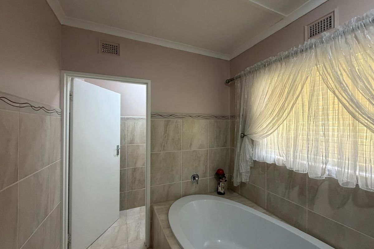 A functional bathroom featuring a built-in bathtub, neutral wall tiling, and a doorway leading to an adjacent space.