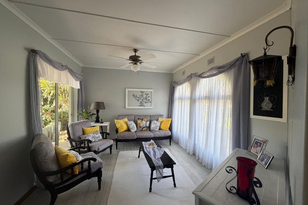 A bright and inviting living room featuring laminate flooring, a ceiling fan, and large windows that provide ample natural light and garden access.