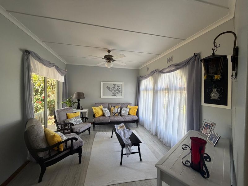 A bright and inviting living room featuring laminate flooring, a ceiling fan, and large windows that provide ample natural light and garden access.