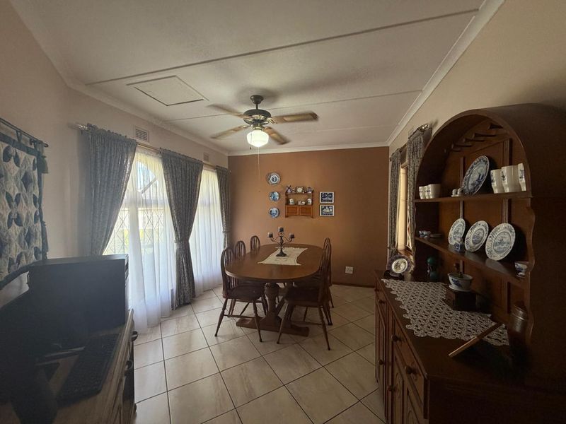 A dining room featuring tiled flooring, a ceiling fan, and large windows with leaded glass detailing.