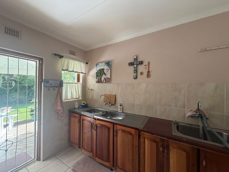 A functional scullery area featuring dual sink stations, wooden cabinetry, and direct access to the outdoor patio area.