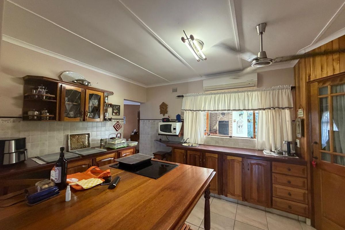 A functional kitchen featuring wooden cabinetry, a central island with a built-in hob, tiled backsplash, and tiled flooring.