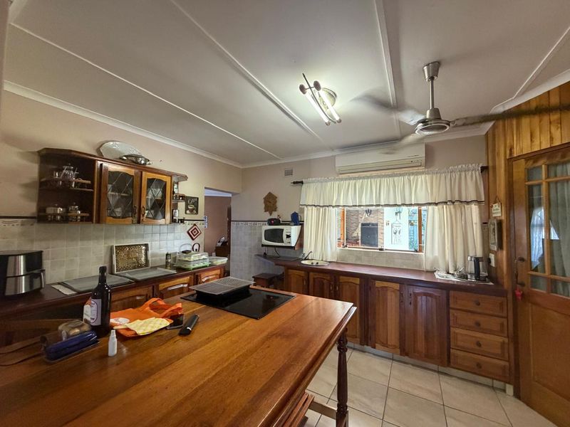 A functional kitchen featuring wooden cabinetry, a central island with a built-in hob, tiled backsplash, and tiled flooring.
