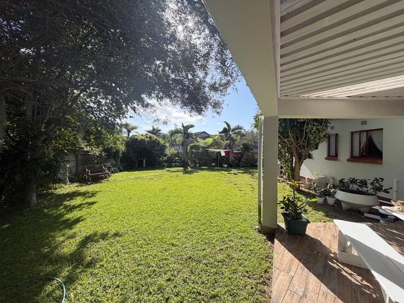 A covered patio area overlooking a spacious, well-maintained garden with mature trees and a lawn.