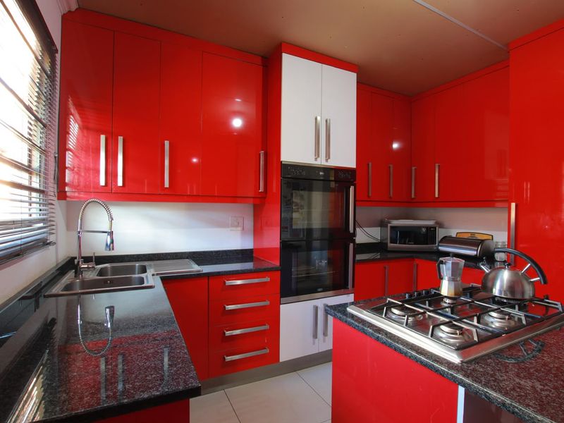 A vibrant kitchen featuring high-gloss red cabinetry, contrasting white accents, granite countertops, a built-in double oven, and a gas hob.