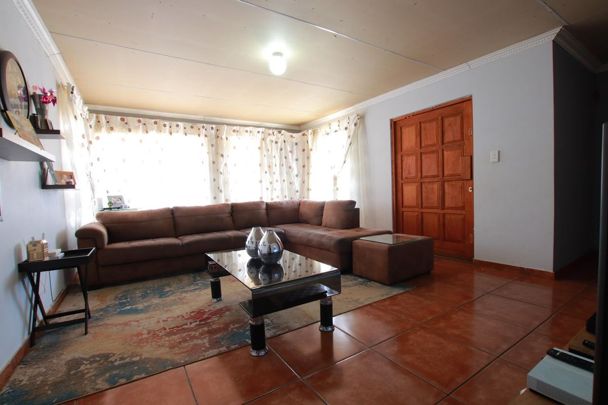 A living room featuring tiled flooring and a wooden panel door, with potential for ceiling improvements to enhance the overall aesthetic.