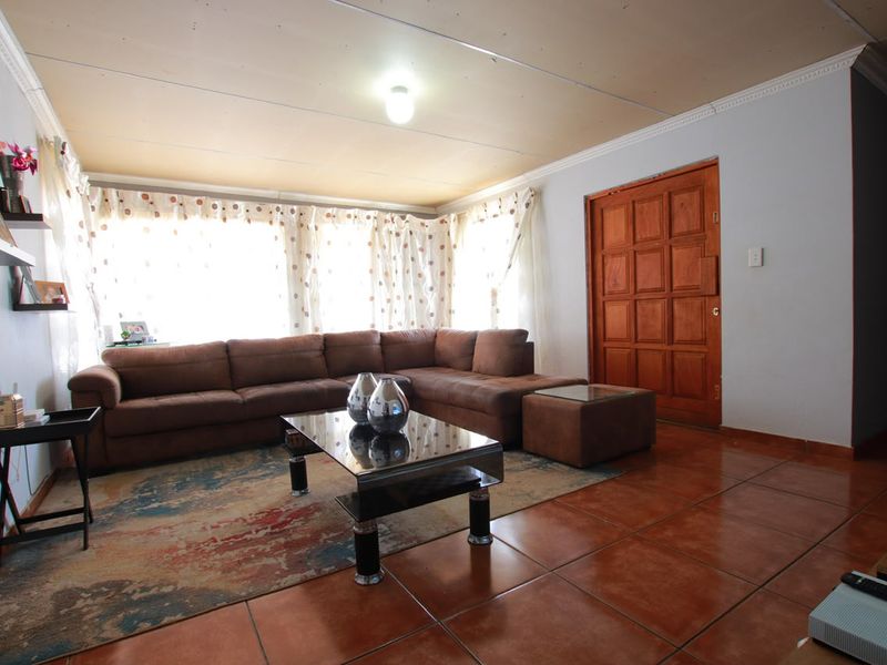 A living room featuring tiled flooring and a wooden panel door, with potential for ceiling improvements to enhance the overall aesthetic.
