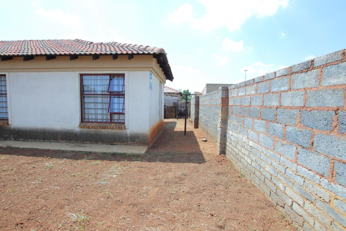 Rear exterior view of the house featuring a tiled roof, security-barred windows, and a concrete block boundary wall with an unlandscaped yard.