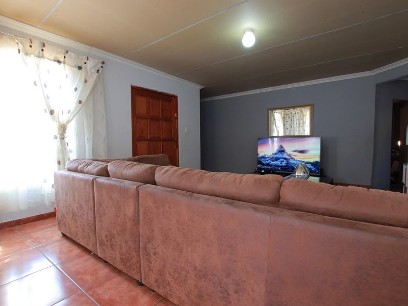 A living room featuring tiled flooring, a timber door, and a ceiling with visible panel joints.