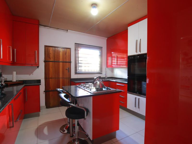 Modern kitchen featuring high-gloss red and white cabinetry, granite countertops, a central island with a gas hob, and built-in oven.