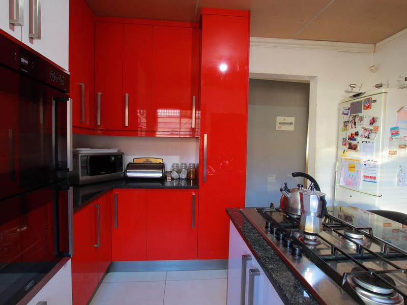 A kitchen featuring vibrant red high-gloss cabinetry, granite countertops, a built-in oven, and a gas hob, with tiled flooring throughout.