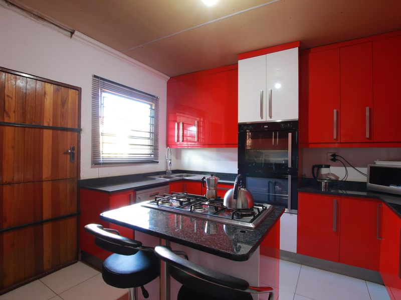 A vibrant kitchen featuring high-gloss red and white cabinetry, granite countertops, a central island with a gas hob, and built-in oven.