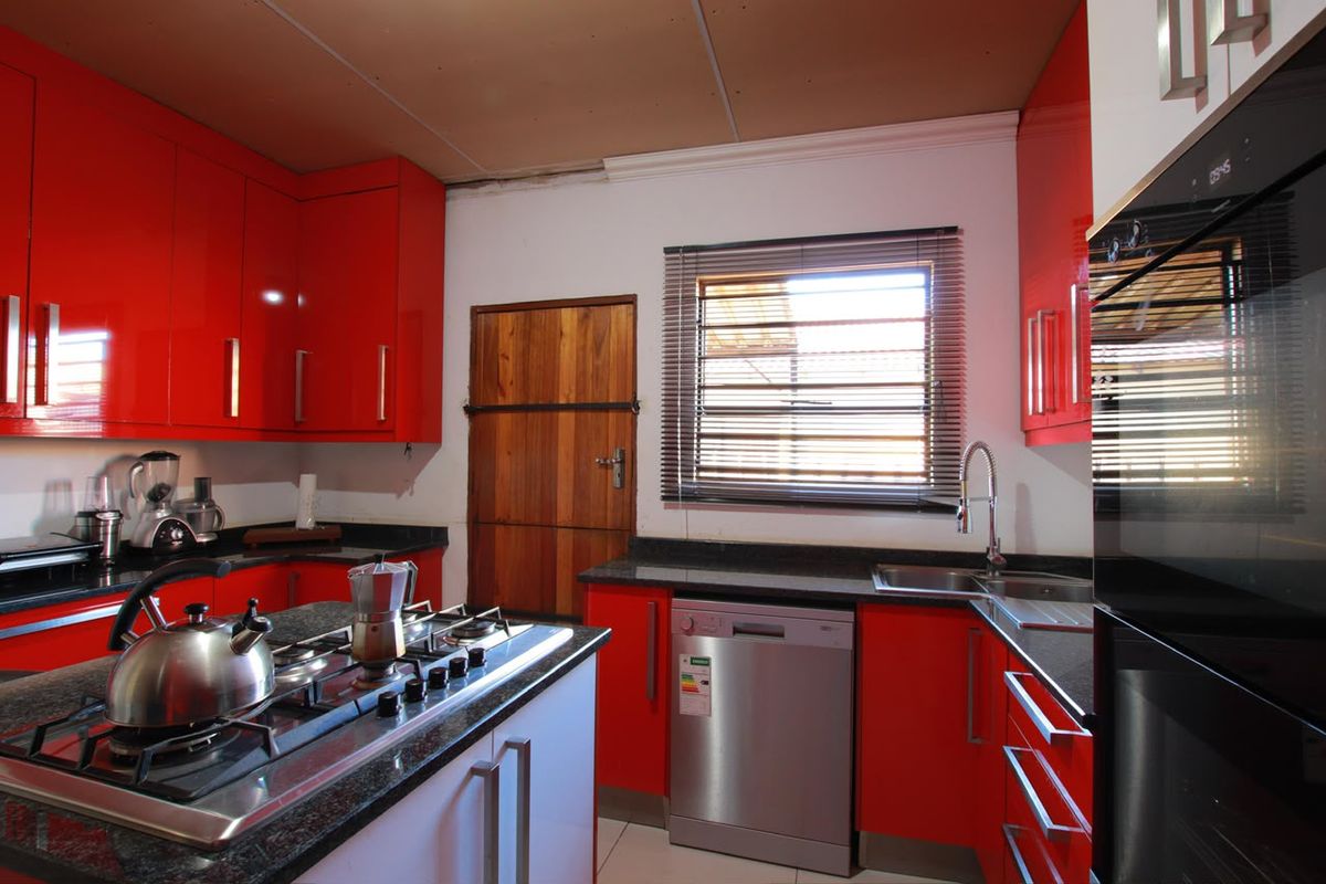 A vibrant kitchen featuring high-gloss red cabinetry, granite countertops, a central gas hob, and integrated appliances, requiring minor ceiling finishing.