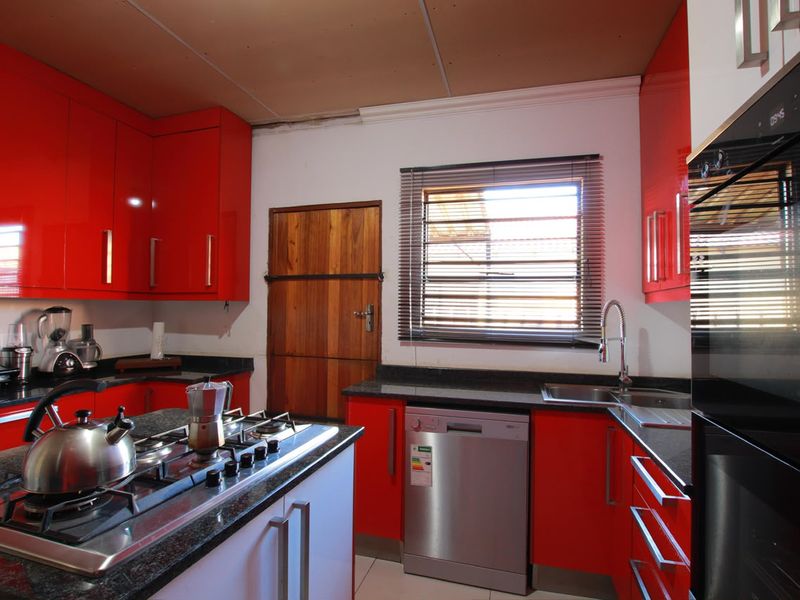 A vibrant kitchen featuring high-gloss red cabinetry, granite countertops, a central gas hob, and integrated appliances, requiring minor ceiling finishing.