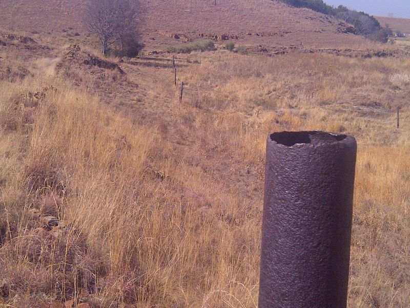 A view of the farm landscape featuring dry grass, wire fencing, and a weathered metal pipe in the foreground.