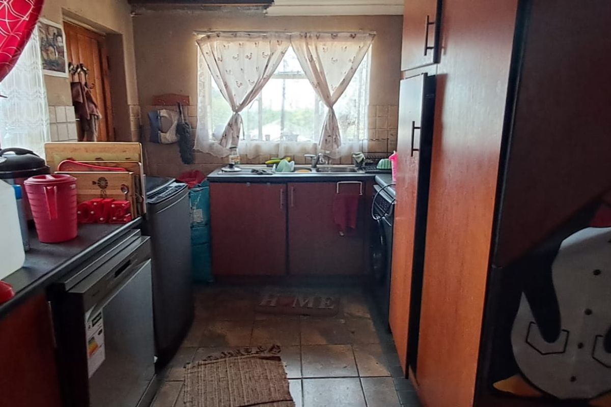 A compact kitchen featuring built-in cabinetry, a double sink, and tiled flooring, currently showing signs of wear and requiring cosmetic updates.
