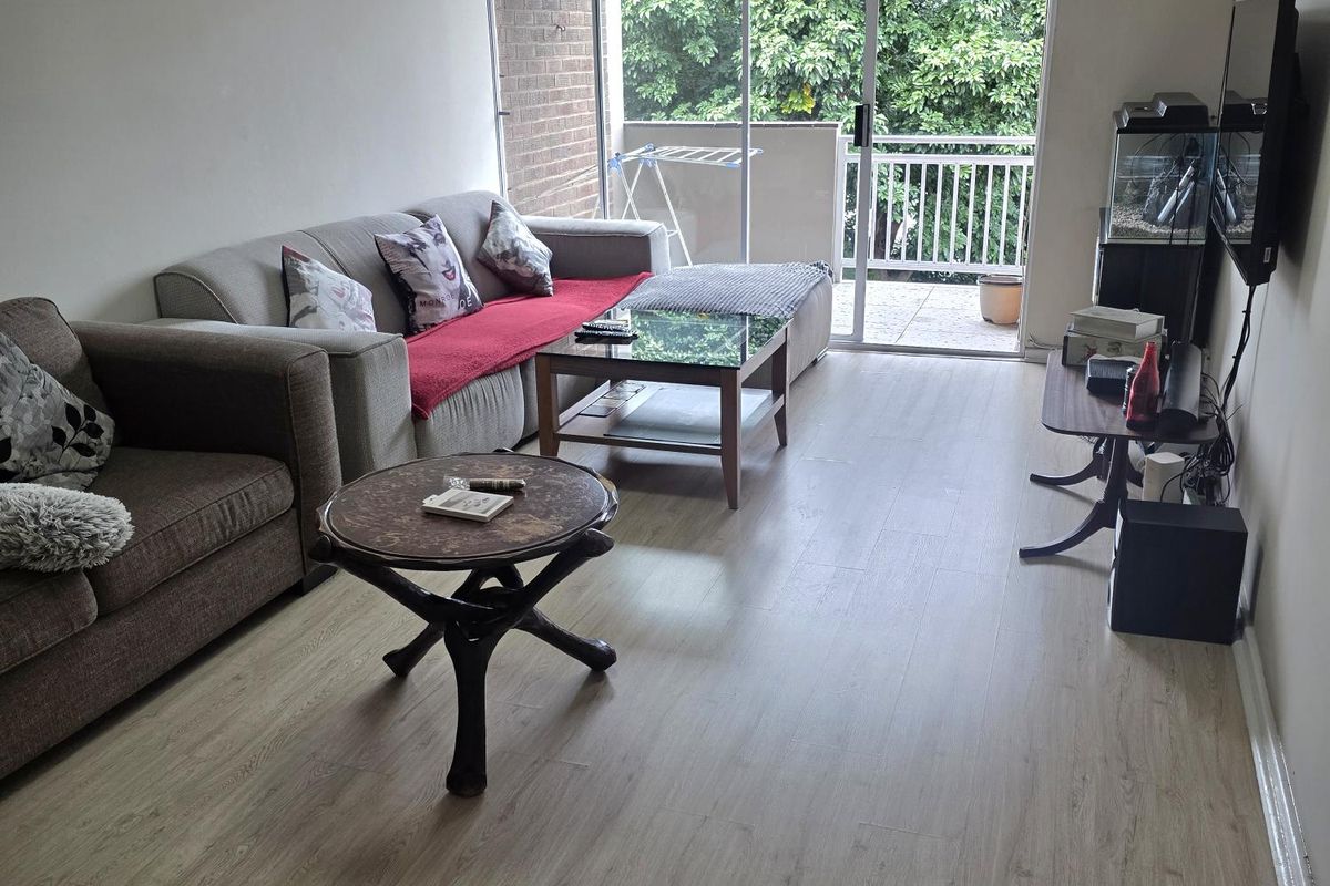 A living room featuring light-toned laminate flooring and a large sliding glass door providing access to an outdoor balcony area.