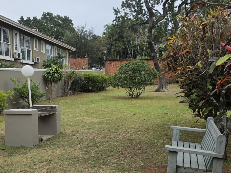 A spacious communal garden area featuring a built-in braai, established trees, and perimeter walling, providing a pleasant outdoor space for residents.