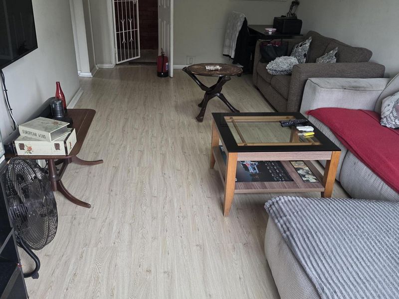 A living room featuring light-toned laminate flooring, a security gate at the entrance, and neutral wall finishes.