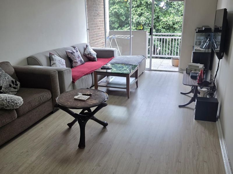 A living room featuring light-toned laminate flooring and a large sliding glass door providing access to an outdoor balcony area.