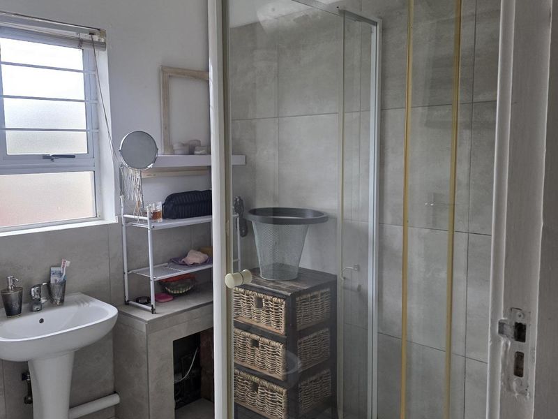 A functional bathroom featuring a pedestal basin, a glass-enclosed shower with tiled walls, and a louver window for ventilation.