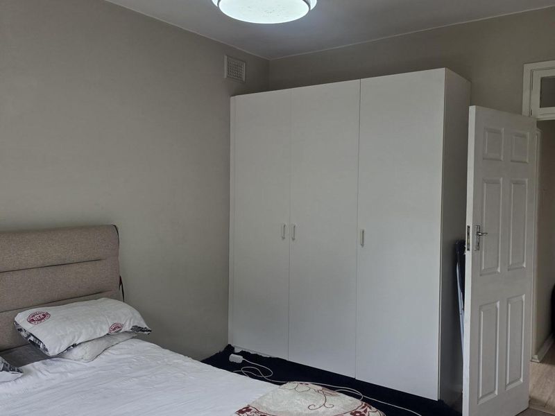 A bedroom featuring a built-in white wardrobe, a modern ceiling fan with light, and neutral wall finishes.