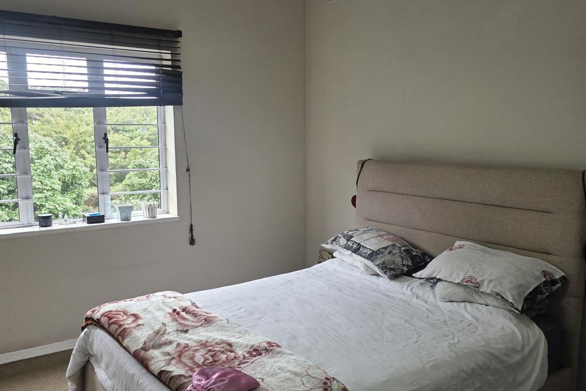A functional bedroom featuring a louvered window, neutral wall finishes, and a ceiling-mounted light fixture.