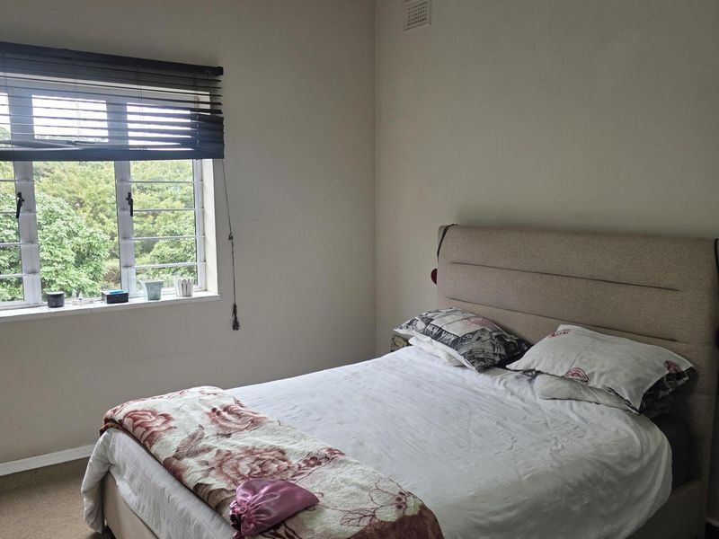 A functional bedroom featuring a louvered window, neutral wall finishes, and a ceiling-mounted light fixture.