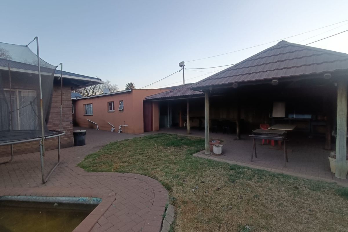Rear exterior view featuring a covered patio area, paved courtyard, and swimming pool set within a private garden space.
