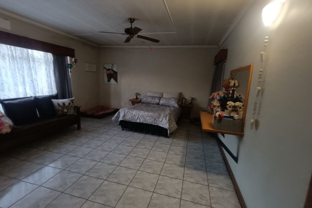 Spacious bedroom featuring tiled flooring, a ceiling fan, and a wall-mounted shelf, offering a functional layout with neutral finishes.