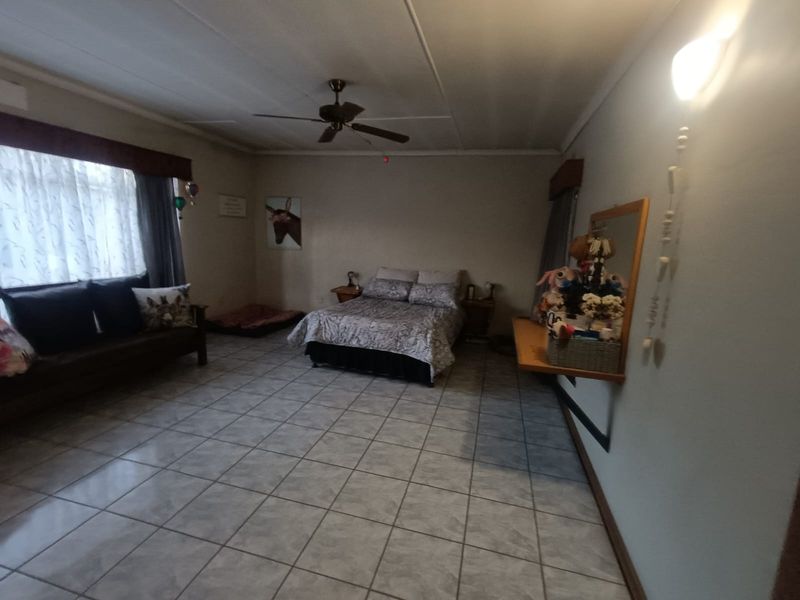 Spacious bedroom featuring tiled flooring, a ceiling fan, and a wall-mounted shelf, offering a functional layout with neutral finishes.