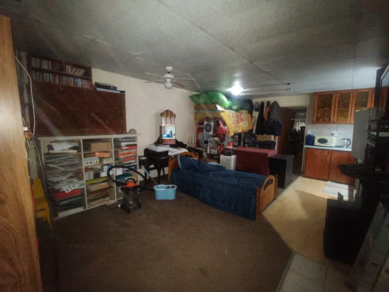 Open plan living and kitchen area featuring ceiling fan, built-in cabinetry, and tiled flooring, currently in need of maintenance and renovation.