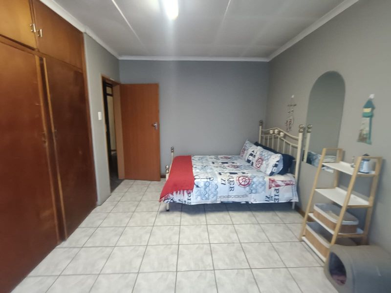 A bedroom featuring tiled flooring, built-in wooden cupboards, and an arched wall mirror, offering a functional space with potential for cosmetic updates.