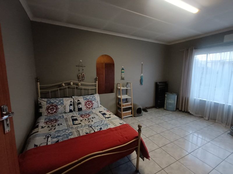 A bedroom featuring tiled flooring, an arch-shaped wall niche, and large windows with curtain rails, offering a functional and neutral living space.